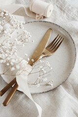 Fototapeta na wymiar Stylish elegant table setting with cutlery, plate, white flowers on beige linen tablecloth background with space for text