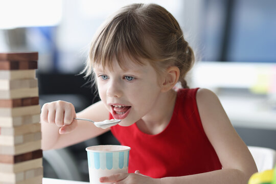 Little Girl Eating Ice Cream With Spoon From Plastic Cup At Home