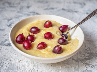Corn porridge with gooseberries, serving in a white plate with a spoon