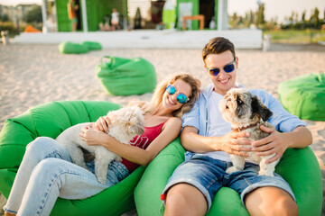 young attractive smiling couple having fun on beach playing with dogs