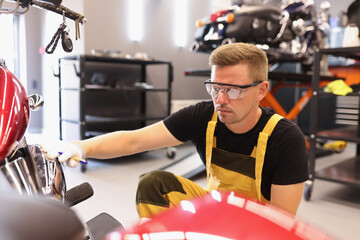Man repairman in goggles picking up paint to motorcycle in car repair shop
