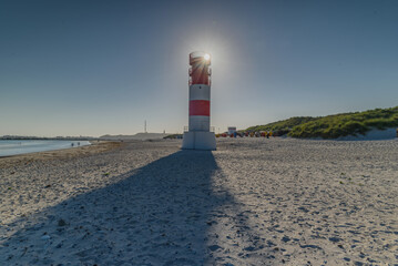 The lighthouse with sunflair glare from behind against brilliant blue sky at Helgoland Düne,...
