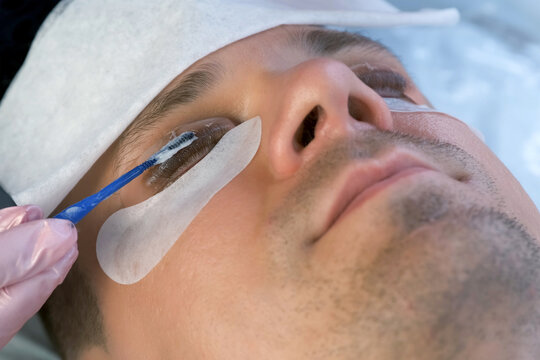 Beautician iss applying solution on man's eyelashes for laminating lifting lash procedure. Cosmetologist is making lash lamination in beauty salon, cosmetology clinic, closeup face of client.