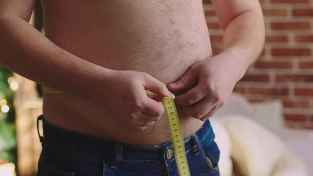Fat adult man measures his large stomach with measuring tape. Closeup. Concept of excess weight and healthy