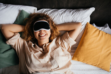 Young beautiful woman wearing sleeping mask relaxing in bed in a bedroom at home.
