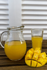 Still life with mango and glass jug with juice on an old wooden background