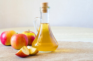 Apple cider vinegar in a glass bottle on a light background with red apples. Malic acid is beneficial for health and is used for cooking. Horizontal orientation