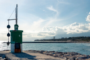 An old unknown structure stands on a pier against the background of the sea, coast and mountains during sunset and white clouds