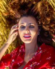 Pretty woman with red curly hair lying on hay outdoors, natural beauty.