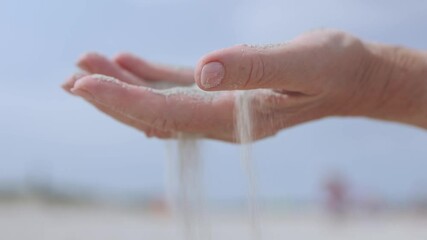elderly senior female palm hand holding and letting go pouring sand through fingers falling down white sand. time passing loss possibilities concept