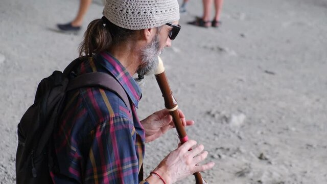 An elderly street musician playing a flute or other wind instrument