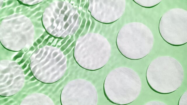 Multiple waves of water create ripples spontaneously on green background with cotton pads | Background shot for face lotion commercial