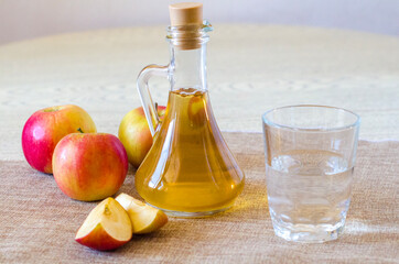 Apple cider vinegar in a glass bottle on a light background with a glass of water. Malic acid is...
