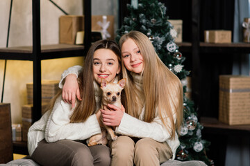 Two cute girls are sitting on a sofa in christmas interior with a Christmas tree. New Year concept
