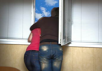 Two lovers look out the window hugging each other - obrazy, fototapety, plakaty