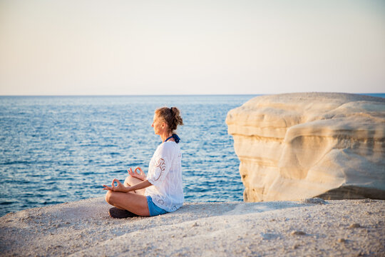 woman in white doing yoga and meditating by the sea