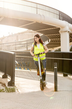 Young girl with reflective vest on electric scooter with bag with shopping in the city. Modern transport concept in the city. Urban lifestyle. New generation, millennial. Ecological transport.