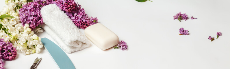 different white toiletries and lilac flowers on a white table. Beauty products for women.