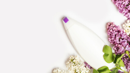 hair care cosmetic products and lilac flowers on white table, flat lay. copy space