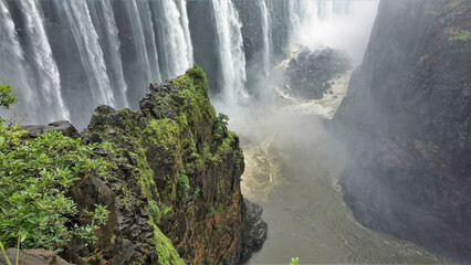 Powerful streams of water fall into the gorge. There is a pile of stones at the bottom. A steep...