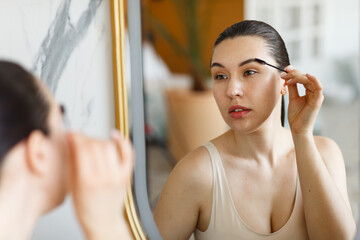 Woman using eyebrow brush near the mirror
