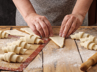 Female hands with wrinkles twist a triangle of dough. Cooking a croissant.