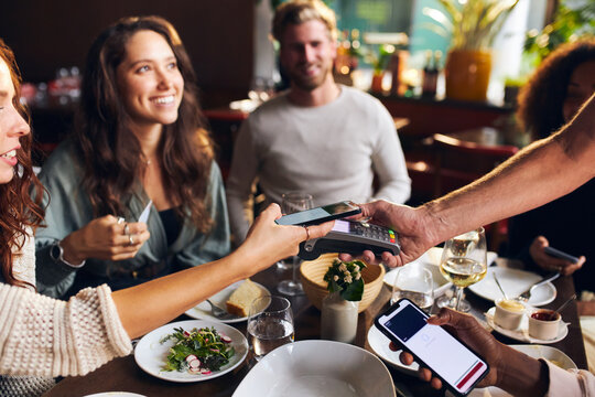 Friends paying contactlessly in restaurant
