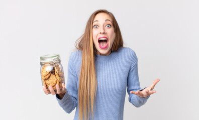 thin pretty woman amazed, shocked and astonished with an unbelievable surprise and holding a cookies