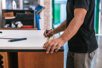 Hand of a man using a pencil to mark a measured point on a surface in a workshop