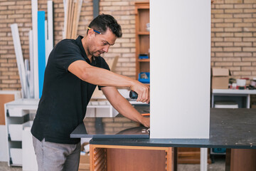 Man fixing a cabinet door with a drill.