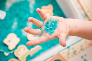 Kid learning numbers through game. Sensory activity with colored rice and wooden numbers. Educations at home, pre-school education, Montessori methodology