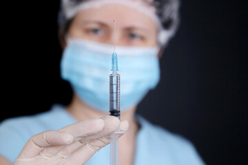 Nurse with syringe, woman in medical mask and protective gloves preparing to injection. Concept of vaccination during covid-19 pandemic