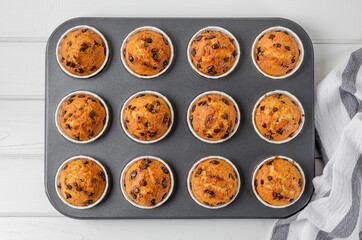 Ready muffins with chocolate chips in baking form on a white wooden background. Recipe step by...