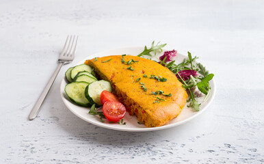 Vegan chickpea omelet with bell peppers served with tomatoes, cucumbers, lettuce and parsley on light gray textured background. Healthy homemade food