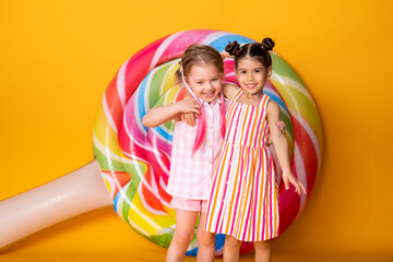 two happy little girls in colorful dress laughing hugging having fun on yellow background