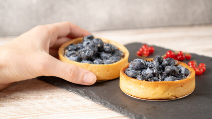 Hand holding blueberry tart. Homemade bilberry tartlets. Fruit dessert with blueberries. Lemon ginger blueberry tart