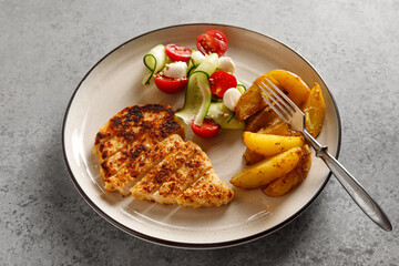Plate with chicken schnitzel with vegetables salad and potatoes on grey table