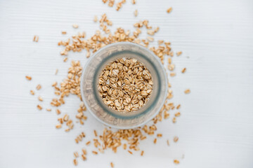 Oatmeal on a white background scattered from a glass jar. Appetizing minimalism