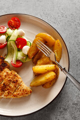 Plate with chicken schnitzel with vegetables salad and potatoes on grey table