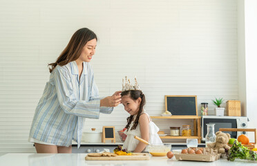 Asian mother wakes up wearing pajamas, makes her daughter's hair happy and has fun. Cracking eggs, baking, mixing ingredients, baking cakes and microwave in the kitchen at home. 