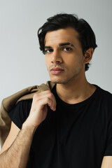 portrait of young man in black t-shirt holding blazer isolated on grey