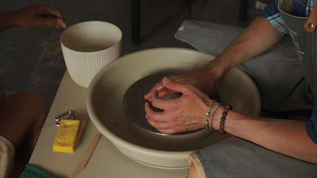 Close-up shot of ceramic cup spinning on potters's wheel and hands molding clay 