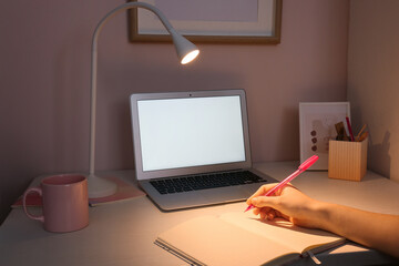 Woman writing in notebook at home late in evening