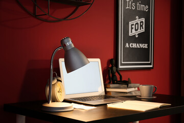 Stylish workplace with modern laptop and glowing lamp near color wall