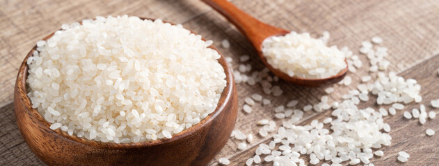 Raw white rice in a wooden bowl over table.