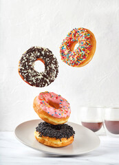 Various decorated, sweet and colorful doughnuts flying or falling into plate. Motion on a white wall background