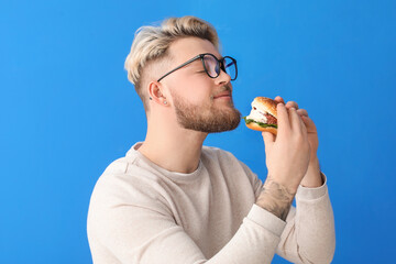Young man eating vegan burger on color background