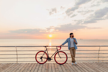 handsome bearded man traveling with bicycle in morning sunrise by the sea