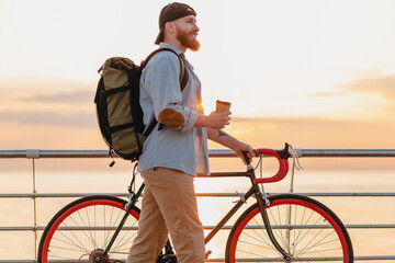 handsome bearded man traveling with bicycle in morning sunrise by the sea