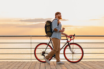 handsome bearded man traveling with bicycle in morning sunrise by the sea